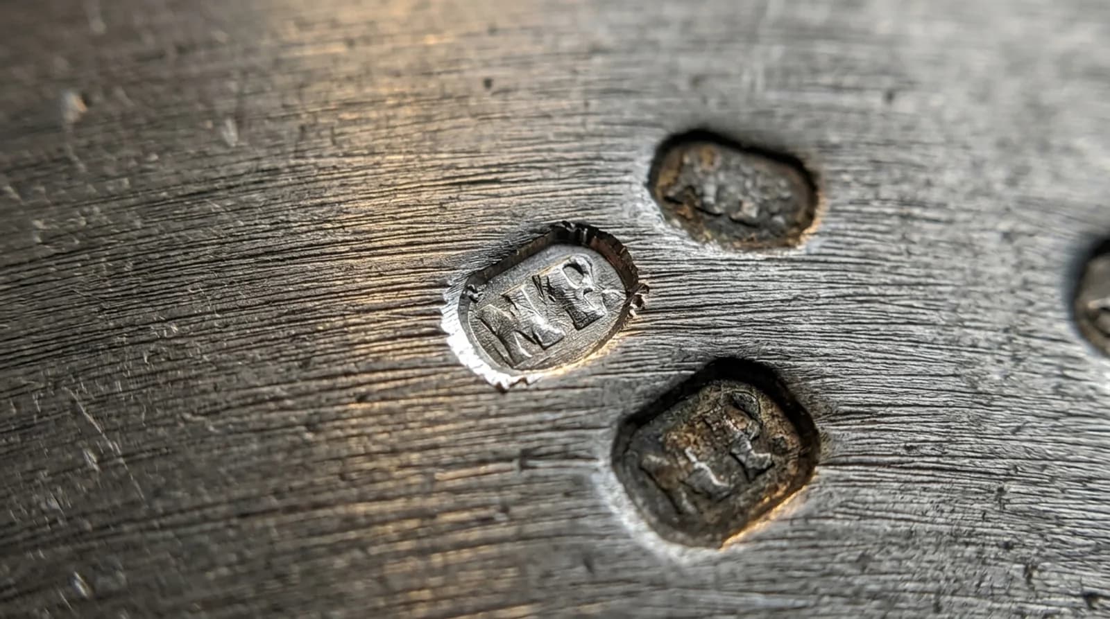 Close-up of brushed pewter with three struck marks, one freshly struck with bright clean edges.